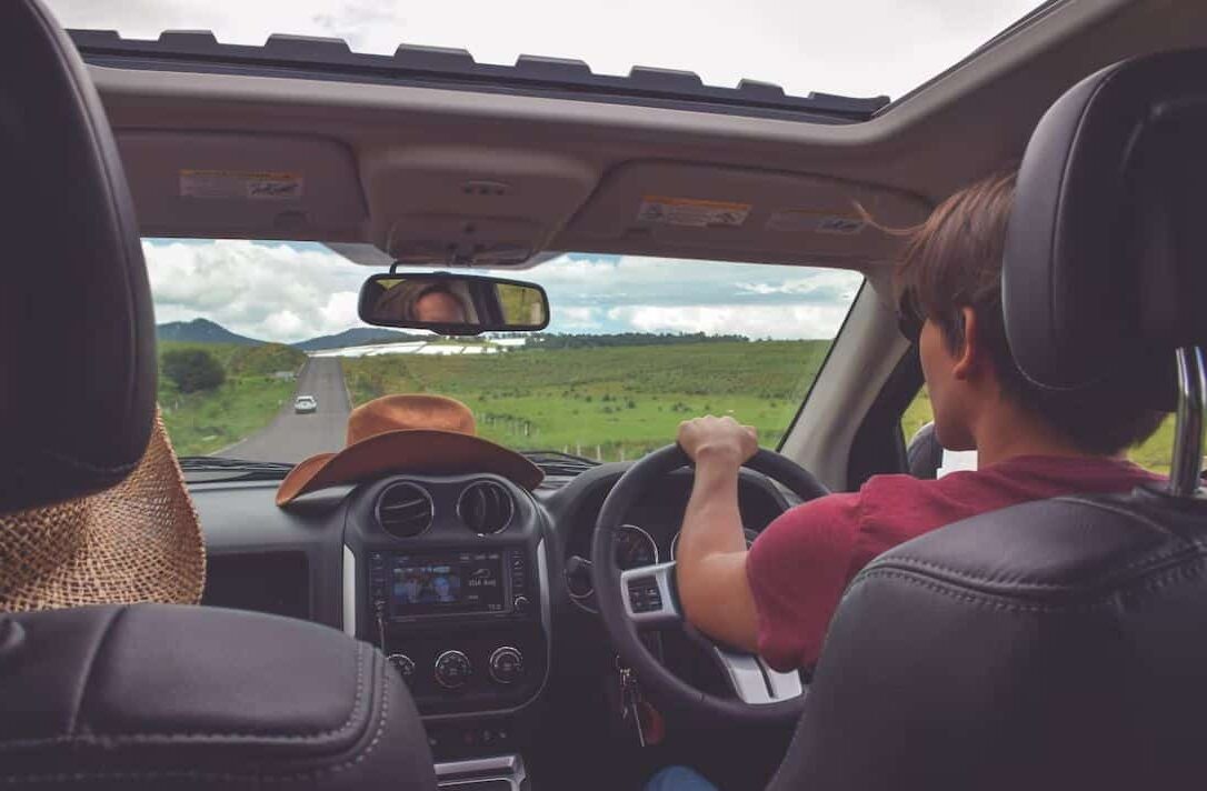 This man driving a country road in a car with a sunroof and a hat on the dash knows how to renew your car insurance and save