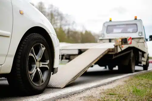 A white car is strategically positioned in front of a tow truck. the driver ready to use their Excess Buster
