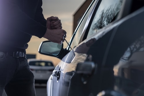 close up of dark car being taken by car thief with screwdriver opening lock in car theft incident