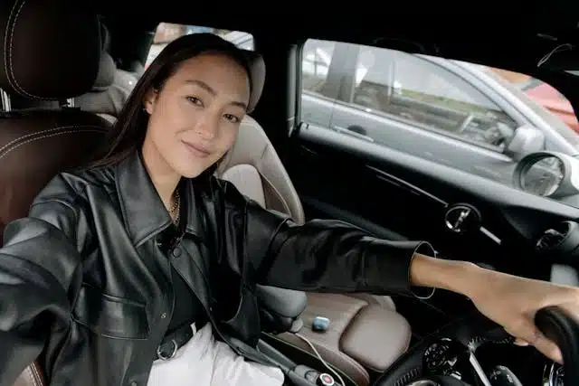 Woman in a leather jacket smiling while enjoying affordable driving in her eco-friendly car.