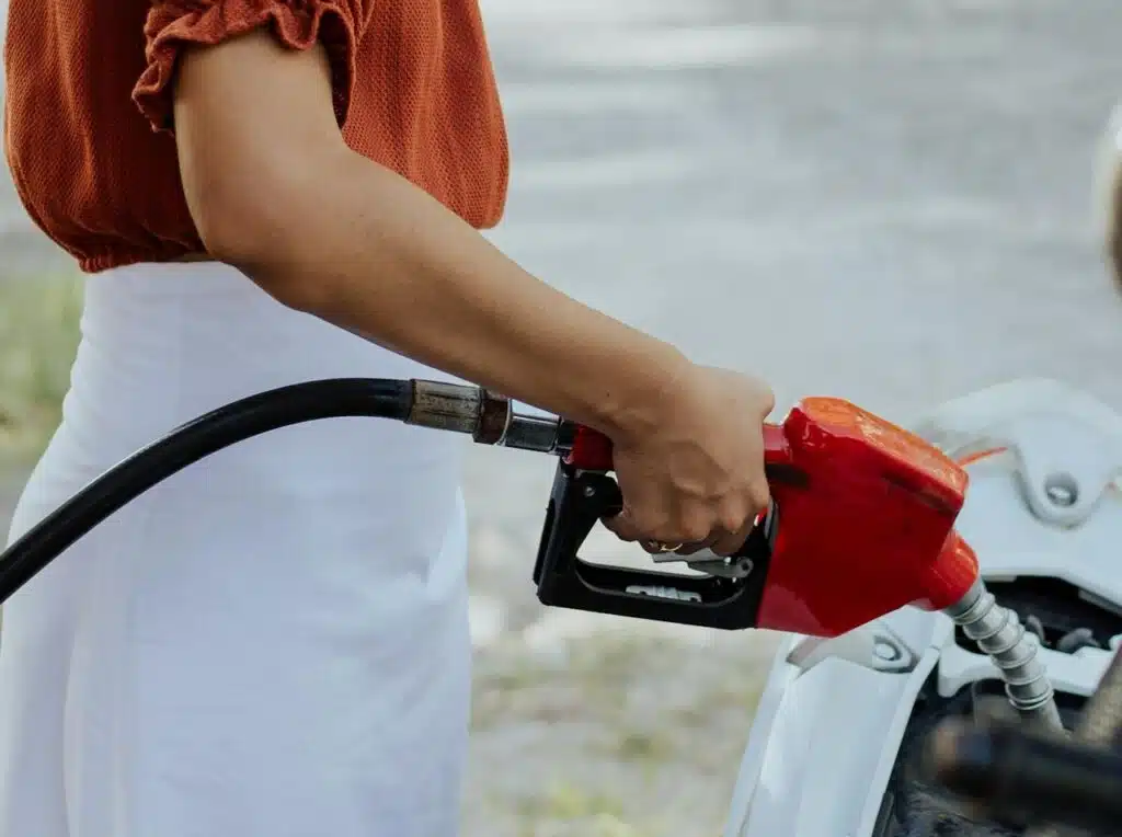 woman in an orange top refueling her car with a vehicle at a gas station.