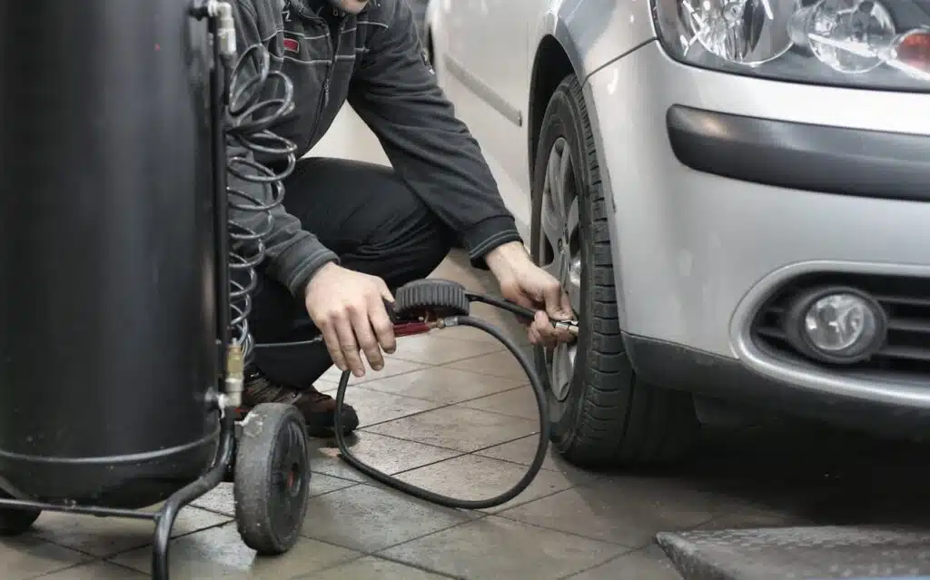 In a well-organized garage, a diligent individual uses an air compressor to inflate a car tire, contemplating how often you should service your car for optimal safety and performance.