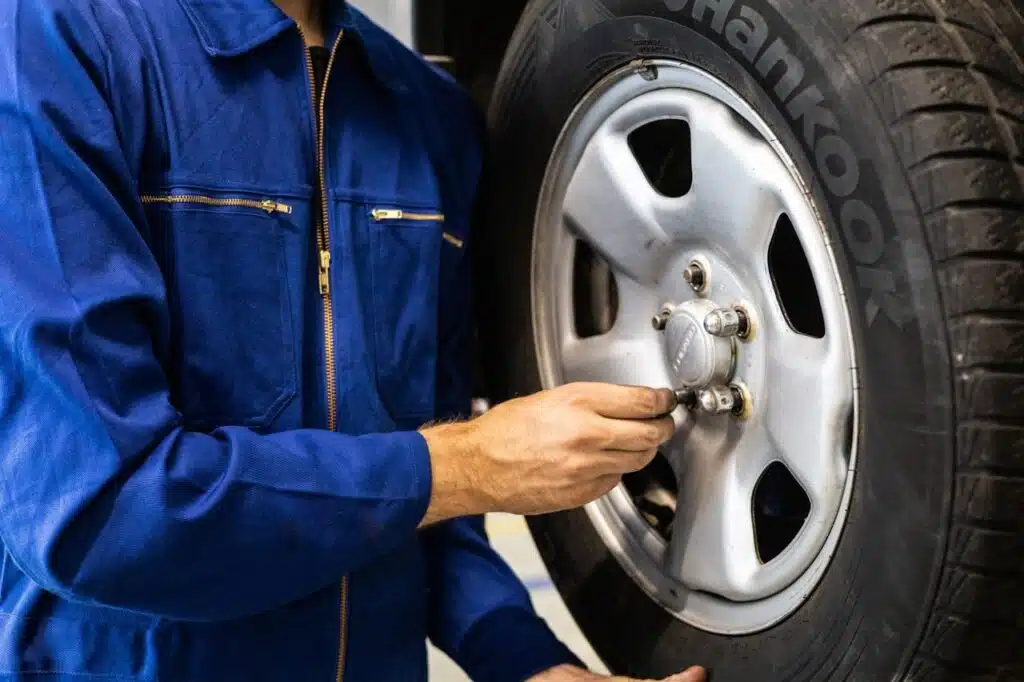 Dressed in a blue coverall, the mechanic skillfully tightens bolts on a car wheel with a ratchet tool, embodying the precision and care that epitomizes Car Servicing.