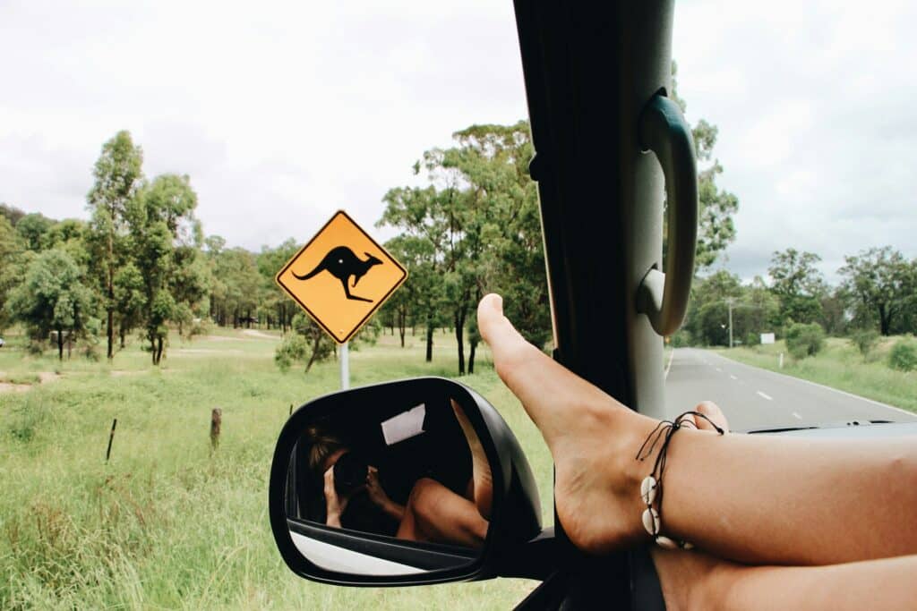 Feet propped up out of the car window, a kangaroo crossing sign in view, perfectly capturing a girls' weekend away in Australia. The open road and lush greenery promise adventure without breaking the bank.