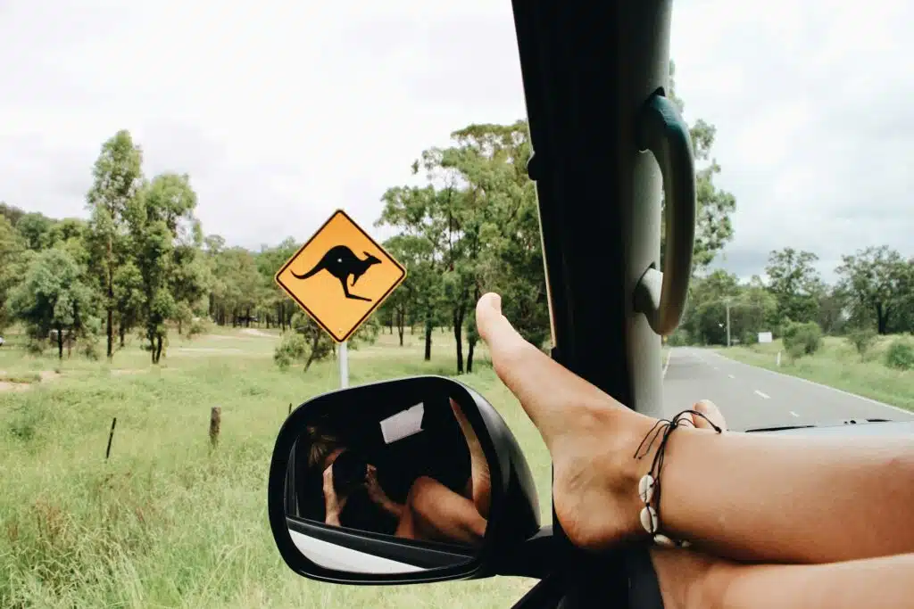 Feet propped up out of the car window, a kangaroo crossing sign in view, perfectly capturing a girls' weekend away in Australia. The open road and lush greenery promise adventure without breaking the bank.