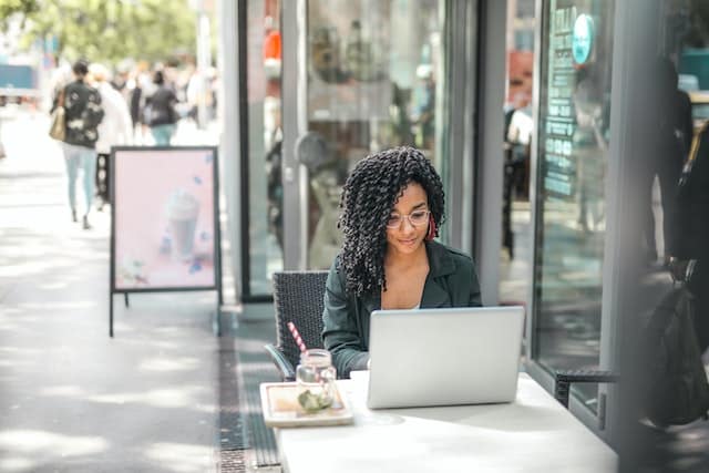 A woman sits on her laptop at a coffee shop, relying on some of the best apps for freelancers to help her work efficiently