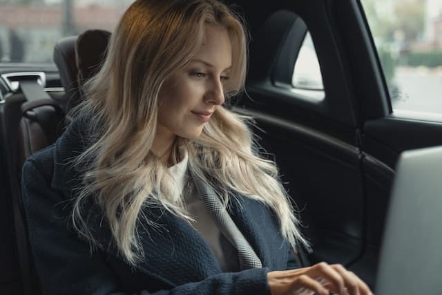 a woman sits in her car researching technology on her laptop
