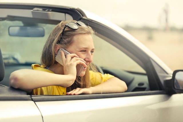 a woman sits in her parked car, chatting on the phone