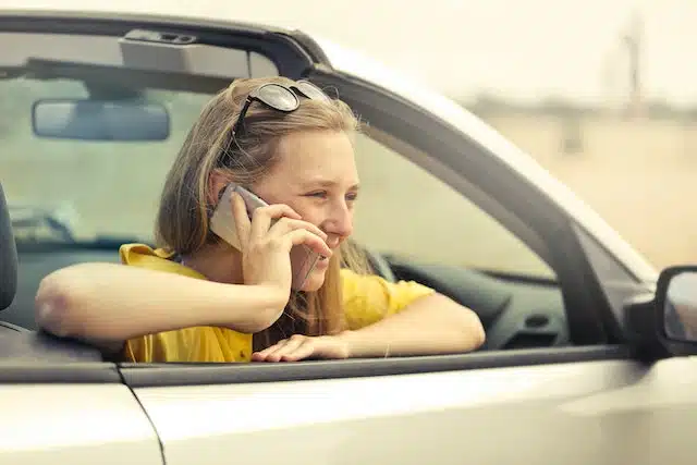 a woman sits in her parked car, chatting on the phone