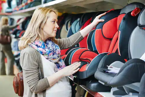 An expecting mother browses different baby car seats in the shopping center with a focus on optimum safety