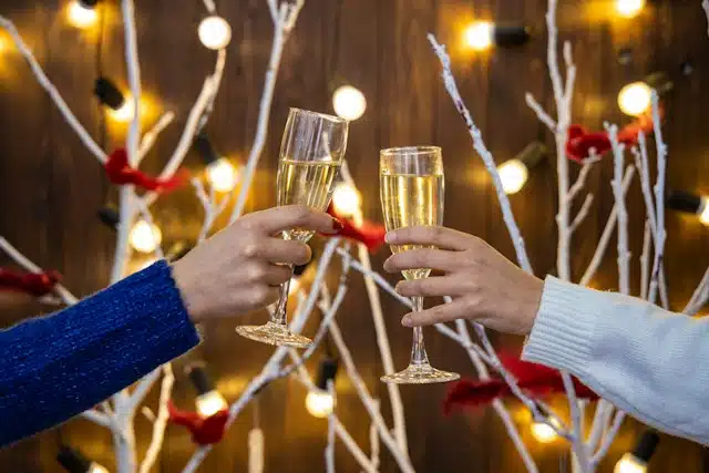 
champagne glasses in women hands on Christmas lights festive room decorated background