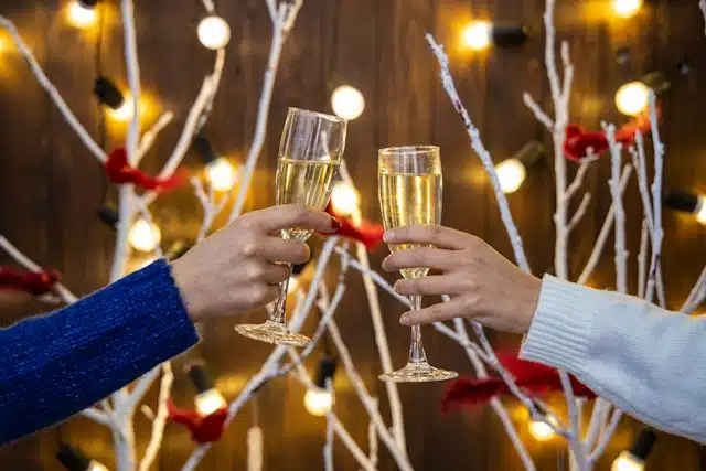 champagne glasses in women hands on Christmas lights festive room decorated background