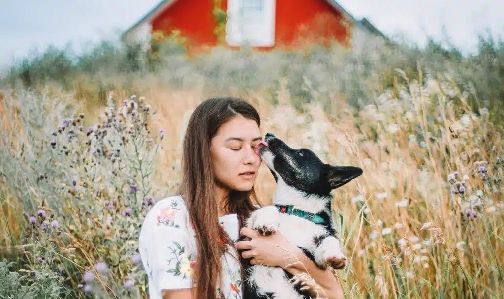 woman stands in long grass and hugs her dog