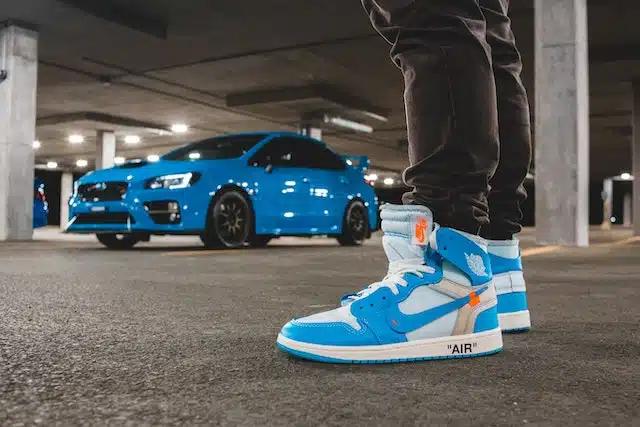 even though it's not illegal to drive in heels this person is opting to wear blue and white sneakers with good grip before getting into their matching blue car in the background