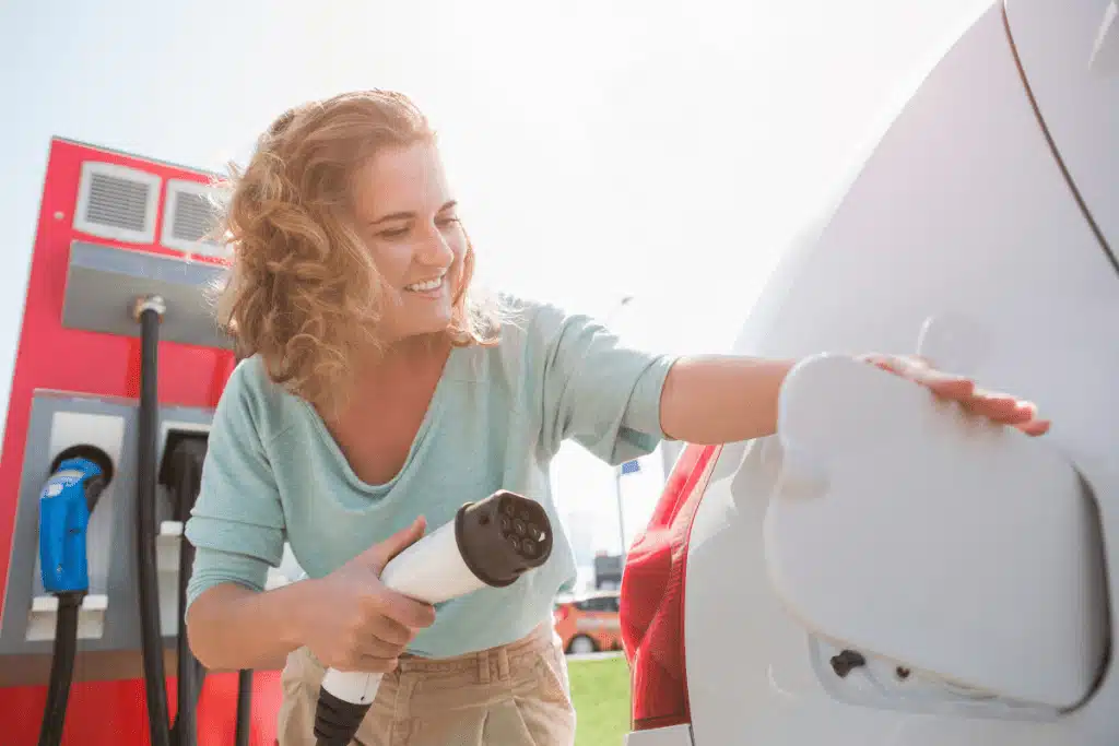 Curly haired woman plugging her car charger in is happy with her choice of the best electric car
