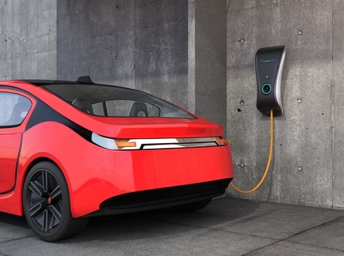 A red electric car, showcasing the future of electric cars in Australia by 2025, is connected to a wall-mounted charging station with an orange cable.