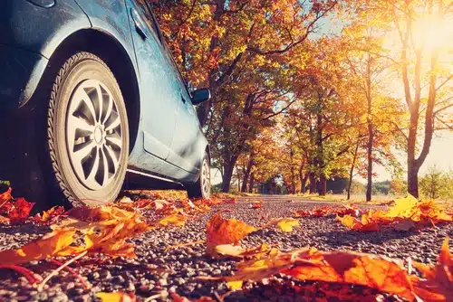 A blue car that's protected by comprehensive car insurance drives through autumn leaves