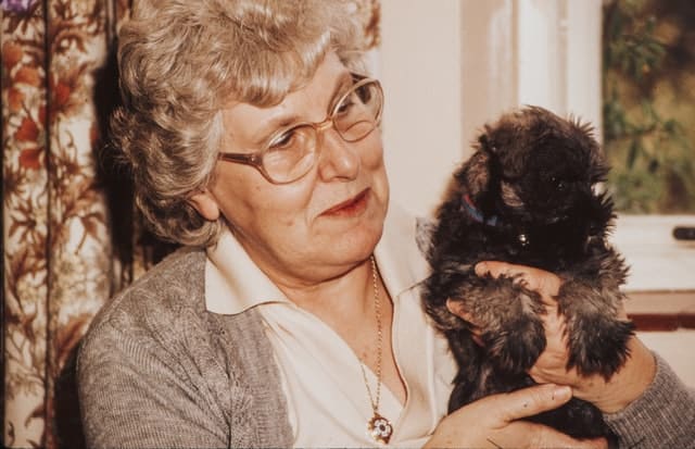 A grandmother pets her young black and white puppy.