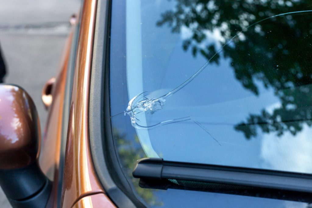 Close-up of a cracked car windscreen on a brown vehicle, reflecting tree branches above.