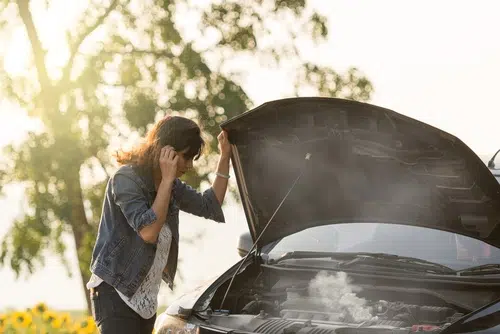 woman standing next to old car overheating on side of road