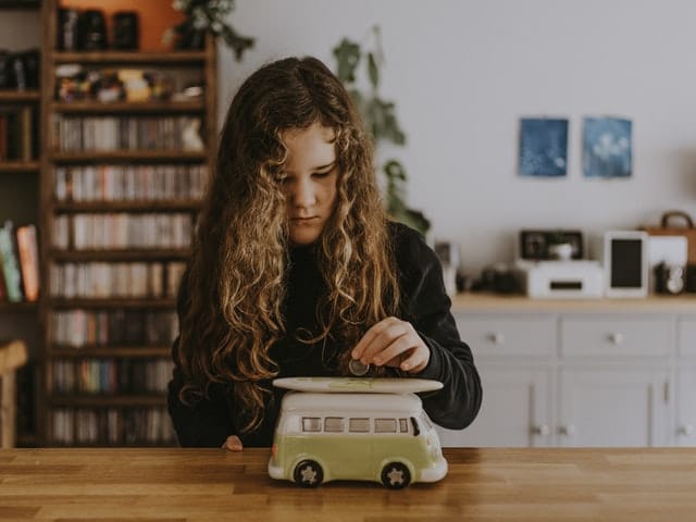 saving for new car - girl putting money into car shaped piggy bank