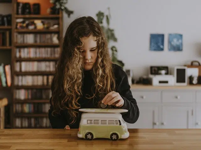 saving for new car - girl putting money into car shaped piggy bank