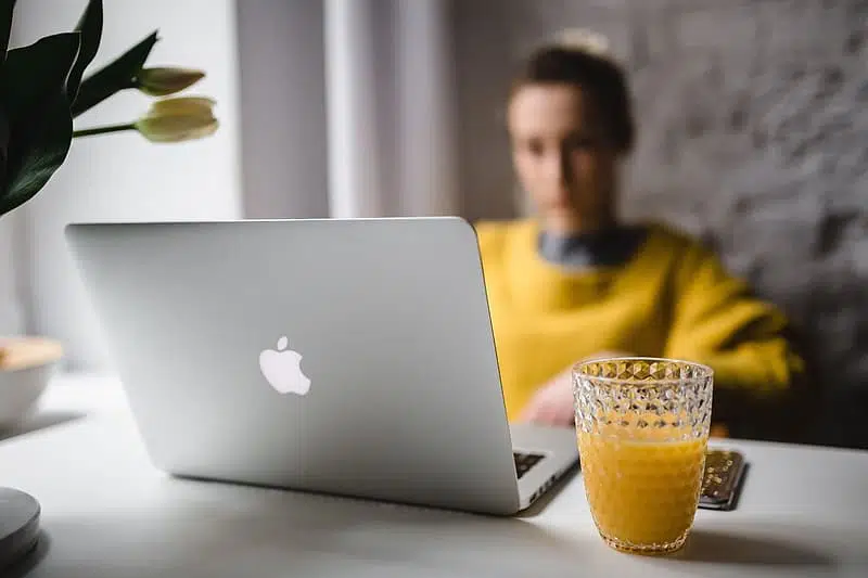 A woman sitting at a desk with an apple laptop and a glass of orange juice, writing her top ten blog posts.