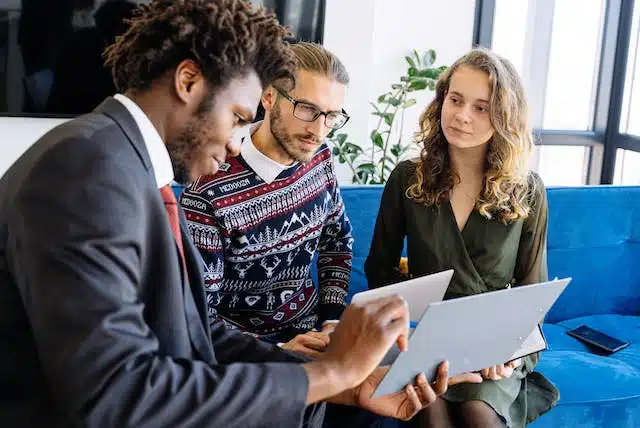 Three business people sitting on a couch looking at a laptop while choosing their excess.
