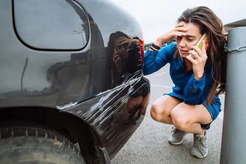 Car Insurance Cost for A New Driver can be expensive. This young driver (who may be unlisted) is staring at a scrape on a car while on the phone 