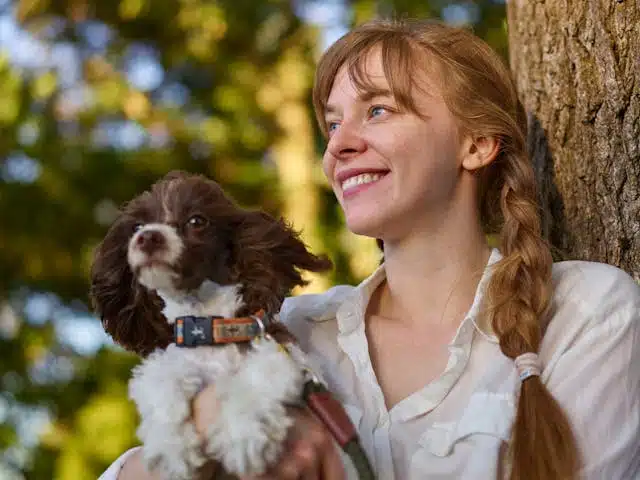 Woman smiling and holding a small rescue dog who enjoys the benefits of not crate training due to past trauma.