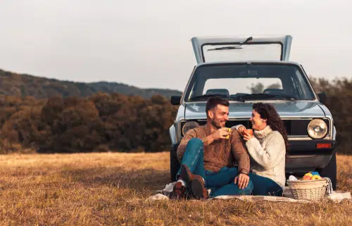couple having picnic in front of blue old high mileage car