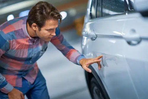 A man inspects the damage to his car and wonders about car scratch repair options.
