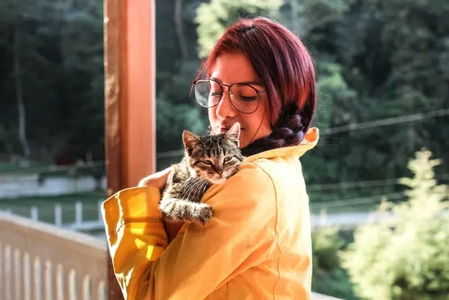 woman in yellow jacket cuddling foster cat on shoulder