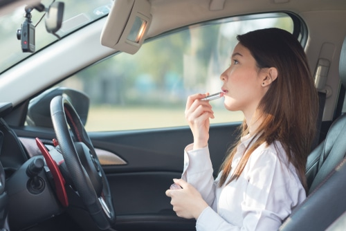 young woman putting on makeup while driving using sun visor mirror