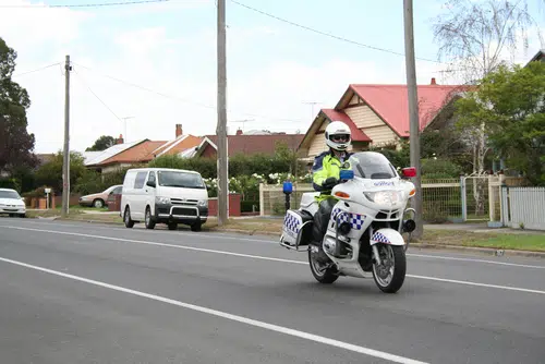 Policeman in yellow vest riding police motorbike in Australia, where random breath testing can take place whenever police decide.