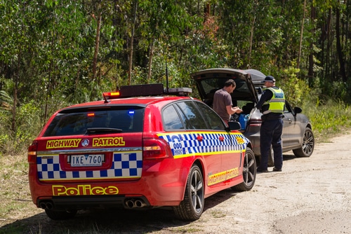 man in grey car pulled over by police highway patrol car on side of road after a car accident