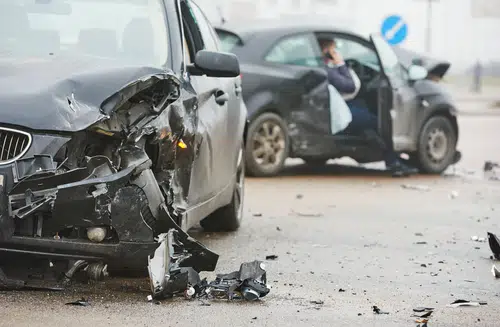 Two black cars damaged after accident. One man on phone with insurance after driving