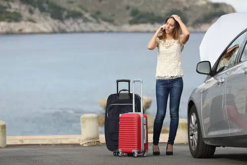 woman next to broken down car making phone call with luggage next to her 