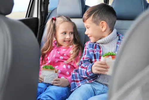 two kids in car with sandwiches as snack