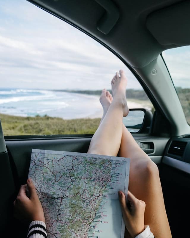 person with map and feet outside of car on holiday roadtrip