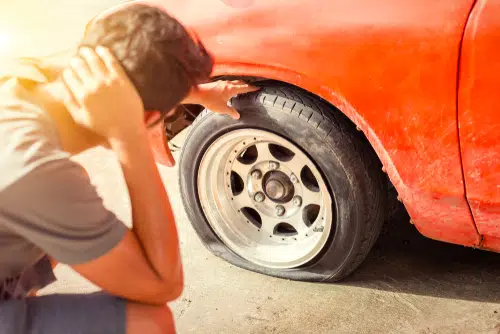 Man with flat tyre - which is a summer driving risk due to increased tyre pressure