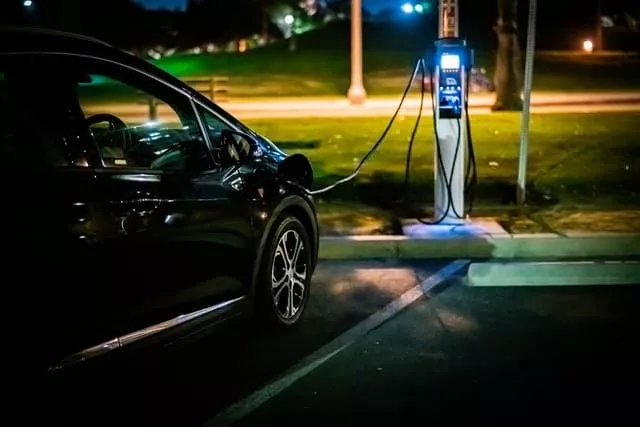 A sleek black Leapmotor electric car is charging at a public station in a well-lit parking area at night, highlighting the shift from petrol to electric. This scene is a glimpse into the future, reminiscent of Australia's anticipated widespread adoption of electric cars by 2025.