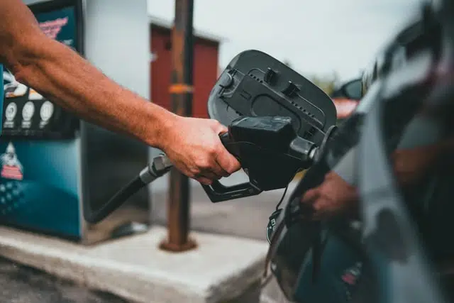 close up of someone holding petrol pump into black car at petrol station filling up with fuel