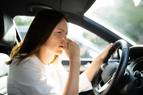 A woman holds her nose while driving.
