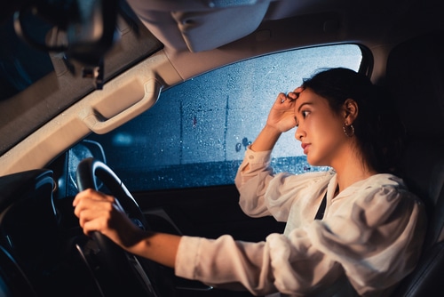 young woman driving car at night in winter rain