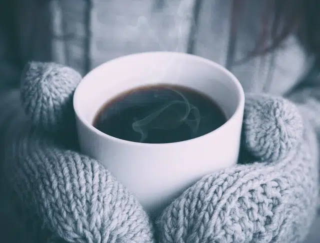 Hands in mittens holding a steaming cup of coffee