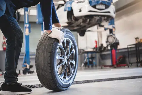 A man is putting a tire on a car in a garage while sharing his expertise in his top ten blog posts for automotive enthusiasts.