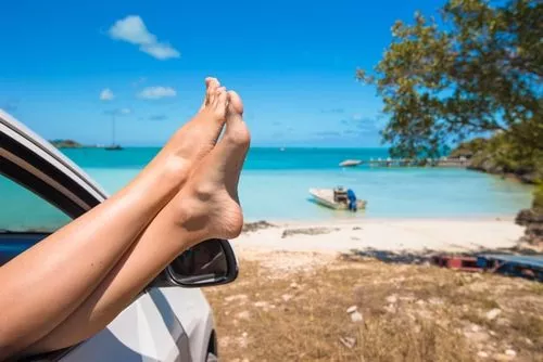 shot of woman's feet hanging out of window of car at the beach