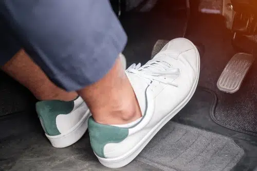 close up of car pedals with man wearing white sneakers. Driving barefoot can be dangerous and closed shoes are the best option
