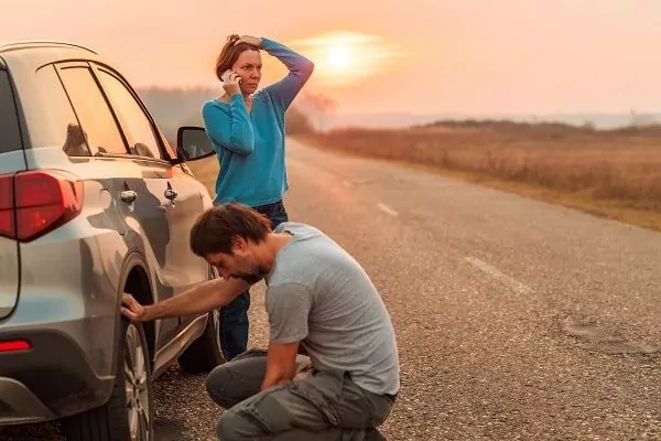Couple repairing car flat tyre on the road, wondering who to call when the car breaks down